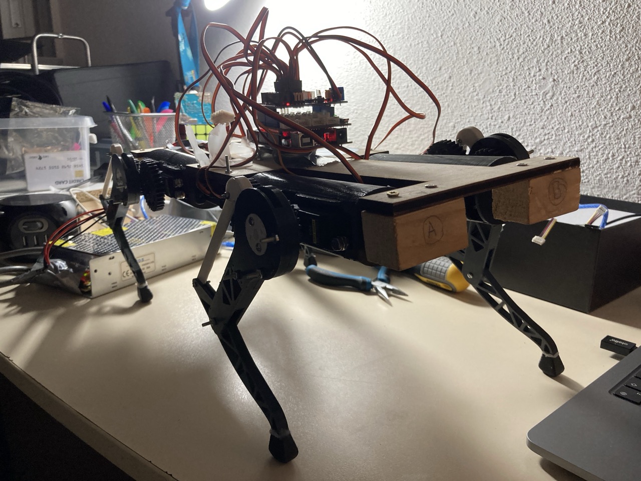 The v0 robot standing on a desk with a huge tangle of red and black servo wires erupting from the stacked control boards on its back — the 'spaghetti' the text is describing.