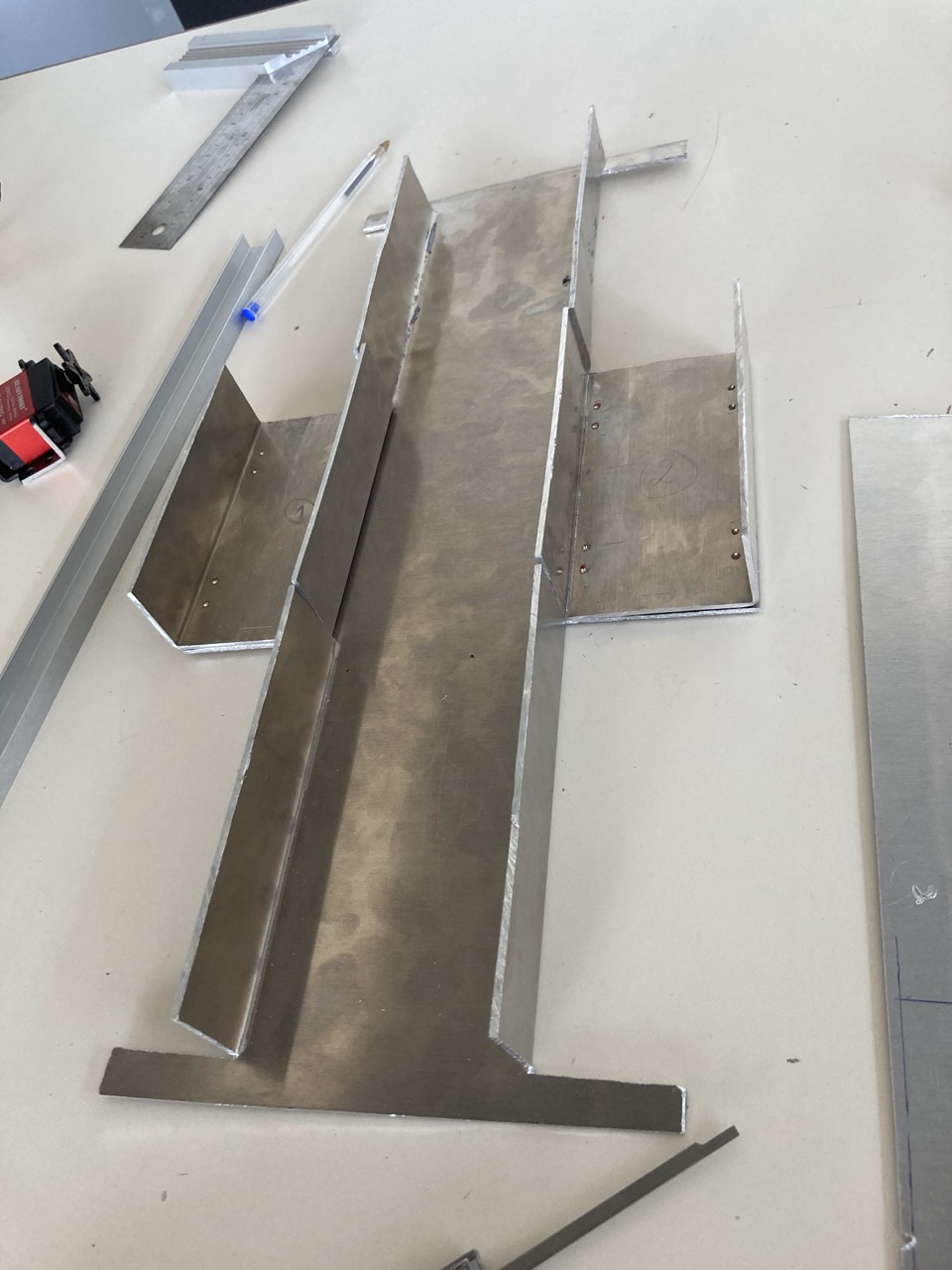 Flat aluminium plates cut and bent into the new chassis pieces, laid out on a workbench with a steel ruler and a pencil.