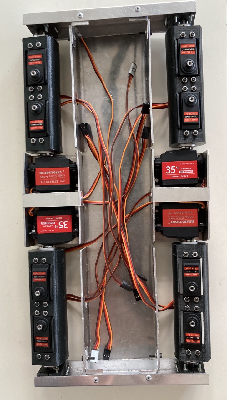 Top-down view of the aluminium frame with all eight servo motors bolted in place along both sides, red 35 kg servos in the middle and orange signal cables gathered down the centre channel.